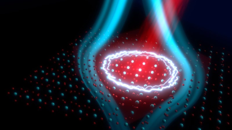 An illustration shows a grid of atoms being hit with a red beam of laser light. Blue lines indicating a magnetic field emanate from the lit-up region.